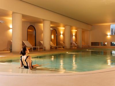 Basen kryty w ciepło oświetlonym hotelu z kolumnami i zrelaksowaną osobą w wodzie.