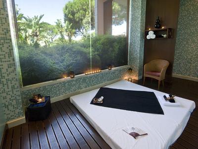 Helles Spa-Zimmer mit Massageliege, Holzboden, Kerzen und großem Fenster mit Naturblick.