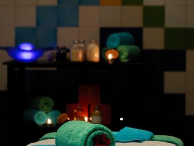 Eine Massagebank mit blauem Handtuch und roten Blüten, im Hintergrund Kerzen und entspannte Atmosphäre.