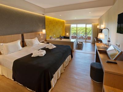 Modernes Hotelzimmer mit Doppelbett, Schreibtisch, bequemen Stuhl und großer Fensterfront zum Balkon.