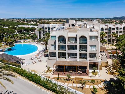 Hotel mit weißen Gebäuden und großem Pool, umgeben von grünen Palmen und blauem Himmel.