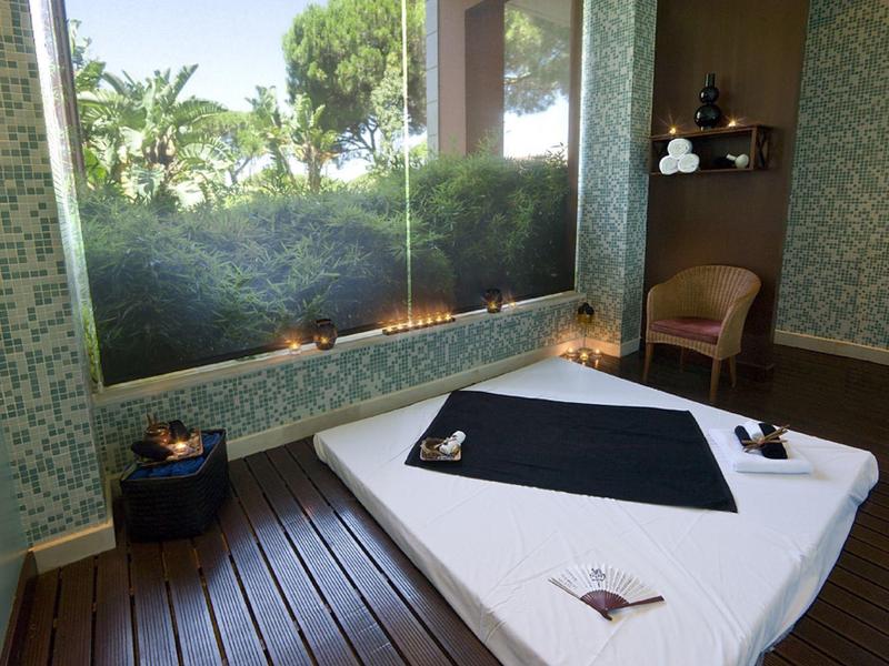 Masážní stůl s uvolněnou atmosférou a výhledem na zelené stromy skrz okno.