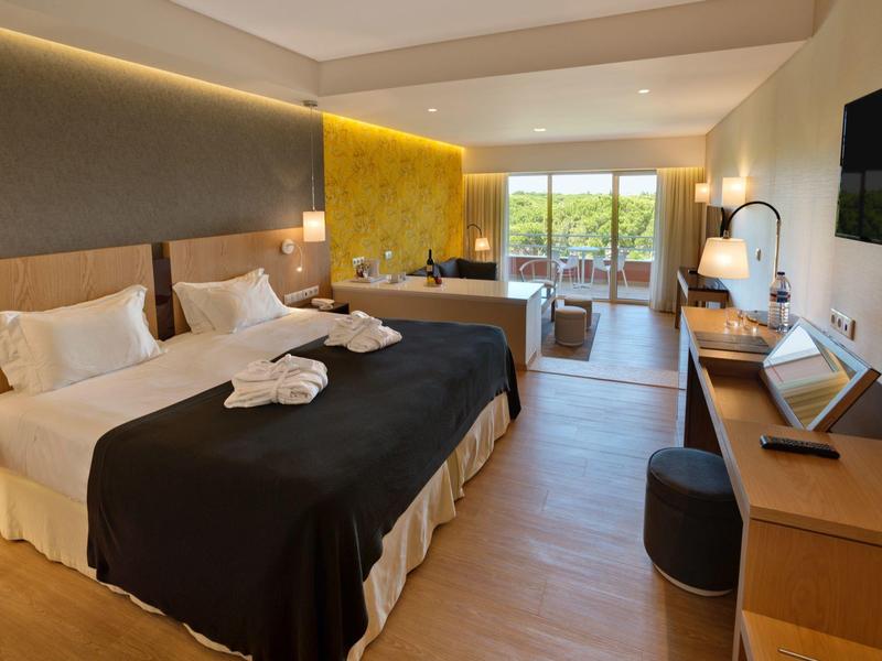 Moderní hotelový pokoj se dvěma postelemi, psacím stolem a přístupem na balkon s výhledem.