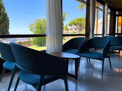 Blaue Sessel mit Holztisch in hellem Raum, große Fenster mit Blick auf Garten und Meer.