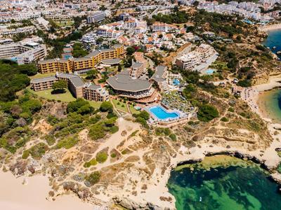 Luftaufnahme einer Küstenstadt mit Sandstrand, Felsen, Hotels und blauem Meer.