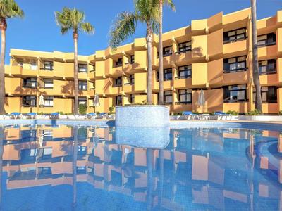 Großes Hotel mit gelben Wänden, Palmen und klarem blauen Pool im Vordergrund.