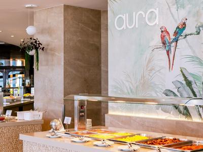 Innenraum eines modernen Restaurants mit Buffet, beige Wänden und buntem Papageien-Wandbild.