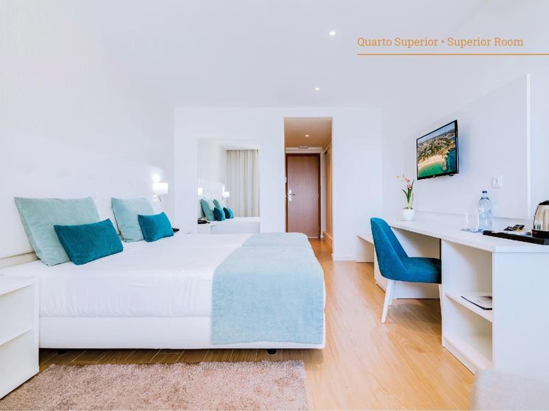 Helles Hotelzimmer mit Doppelbett, türkisfarbener Bettdecke, Schreibtisch, Stuhl und modernem Dekor.