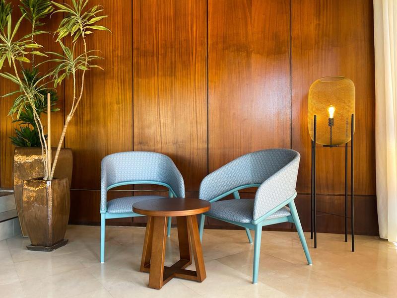 Zwei blaue Stühle mit kleinem runden Holztisch, Stehlampe und große Pflanze vor Holzpaneelen.