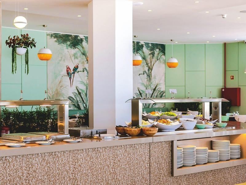 Elegantes Restaurant mit Buffet, grünen Wänden und hängenden Pflanzen, hellem Tageslicht.