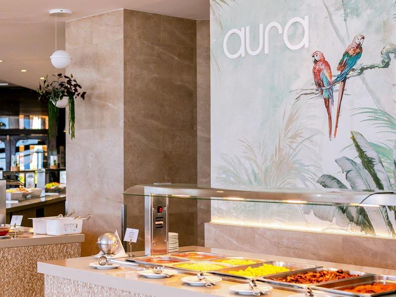 Innenraum eines modernen Restaurants mit Buffet, beige Wänden und buntem Papageien-Wandbild.