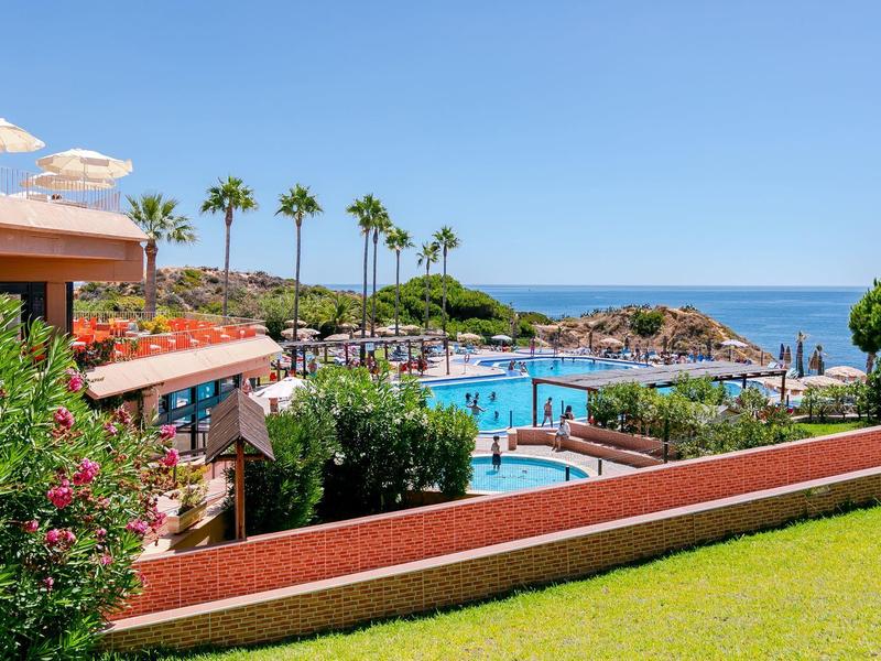 Hotelanlage mit großen Pools, Palmen, grünen Gärten und Blick auf das blaue Meer unter klarem Himmel.