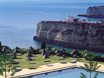 Piscina con ombrelloni e scogliere rocciose vicino al mare calmo sotto cielo azzurro