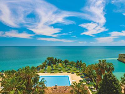 Grande piscina con area circostante e vista sul mare sotto un cielo blu con nuvole.