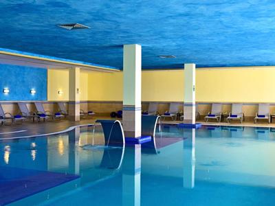 Interno di una piscina con soffitto blu, pareti gialle e sdraio lungo i lati.