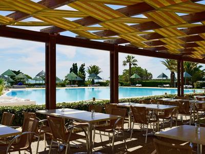 Terrazza coperta con sedie e tavoli con vista su una piscina e piante tropicali.