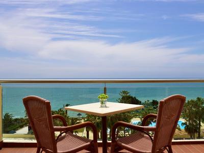 Tavolo sul balcone con due sedie che si affacciano sul mare sotto un cielo sereno.
