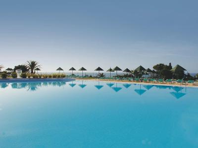 Grande piscina con ombrelloni e lettini sotto un cielo sereno in un resort.