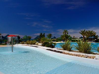 Grande piscina con acqua limpida circondata da piante tropicali e cielo blu.
