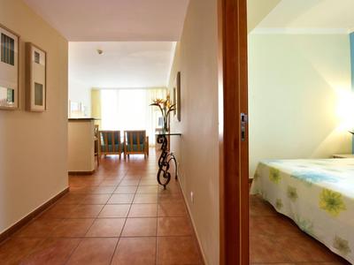 Corridoio ben illuminato con piastrelle marroni e vista su una camera da letto con accento blu.