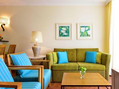 Soggiorno luminoso con divano verde, poltrone blu e tavolo in legno con vaso.