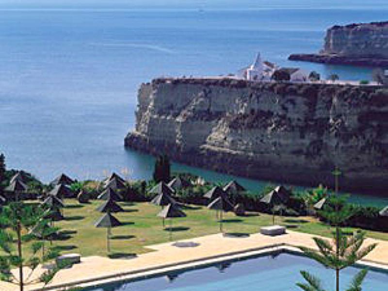 Piscina con ombrelloni e scogliere rocciose vicino al mare calmo sotto cielo azzurro