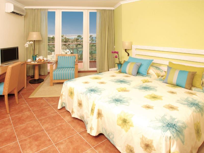 Camera d'hotel luminosa con letto matrimoniale, scrivania, TV e balcone con vista sulla città.