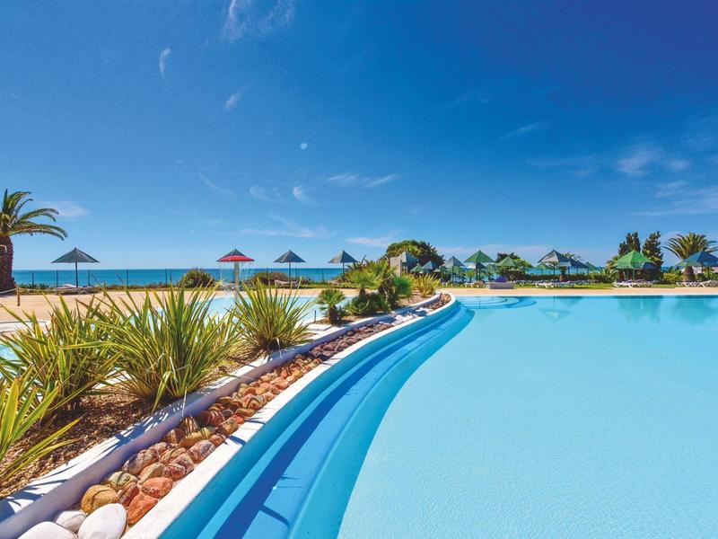 Grande piscina all'aperto con palme, lettini e cielo azzurro limpido vicino al mare.