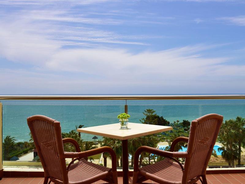 Tavolo sul balcone con due sedie che si affacciano sul mare sotto un cielo sereno.