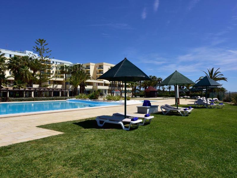 Piscina dell'hotel con lettini e ombrelloni su prato davanti all'edificio sotto cielo sereno.