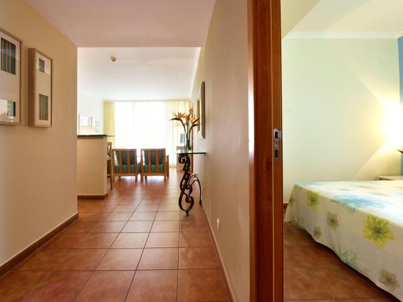 Corridoio ben illuminato con piastrelle marroni e vista su una camera da letto con accento blu.