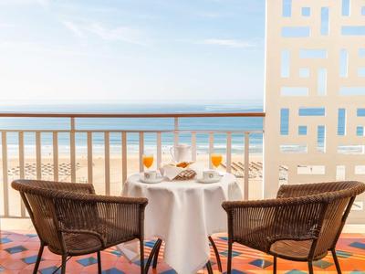 Balcone con tavolo, due sedie e vista mare in una giornata soleggiata.