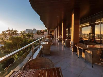 Balcon d'hôtel avec tables et chaises surplombant la mer au coucher du soleil.
