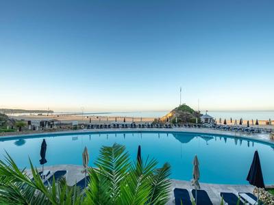 Grande piscine avec transats et vue sur la mer sous un ciel clair.