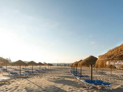 Plage de sable vide avec parasols et transats sous un ciel dégagé.