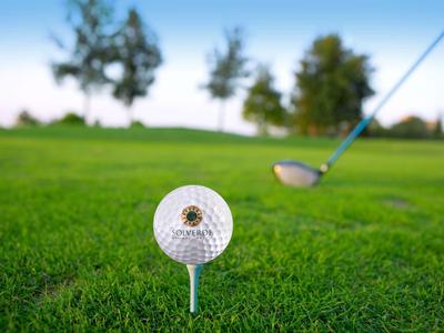 Golfball auf einem Abschlag mit Golfschläger im Hintergrund auf grünem Rasen.