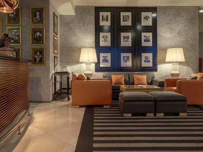 Un espace lounge d'hôtel élégamment aménagé avec des fauteuils, des canapés, des lampes et un mur décoré de tableaux.