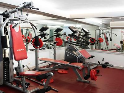 Moderner Fitnessraum mit verschiedenen Trainingsgeräten und großen Spiegeln an der Wand.