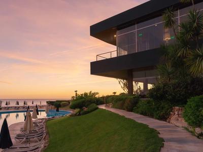 Hôtel moderne avec piscine et terrasse au coucher du soleil donnant sur la mer.