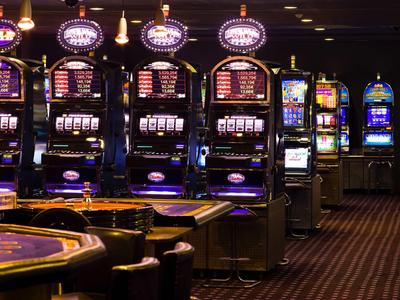 Dunkler Spielsalon mit mehreren beleuchteten Spielautomaten und Karten-Tisch.