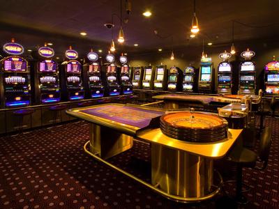 Innenansicht eines Casinos mit Spielautomaten und Spieltischen in gedämpftem Licht.