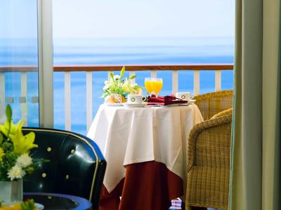 Petite table avec petit-déjeuner et boissons sur balcon avec vue sur la mer.