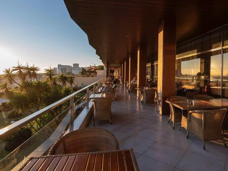 Balcon d'hôtel avec tables et chaises surplombant la mer au coucher du soleil.
