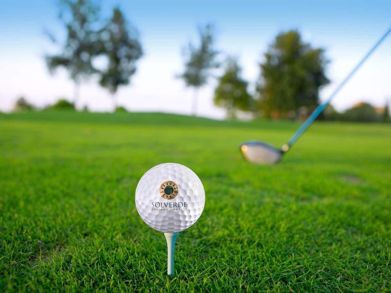 Gros plan d'une balle de golf sur un tee avec un club de golf en arrière-plan sur de l'herbe verte.