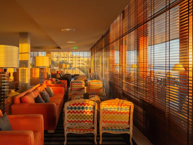 Salon d'hôtel confortable avec canapés et fauteuils, lumière chaude filtrant à travers les stores.