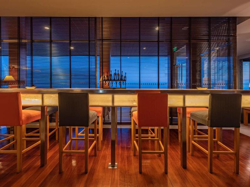 Bar d'hôtel moderne avec des tabourets hauts et de grandes fenêtres au crépuscule.