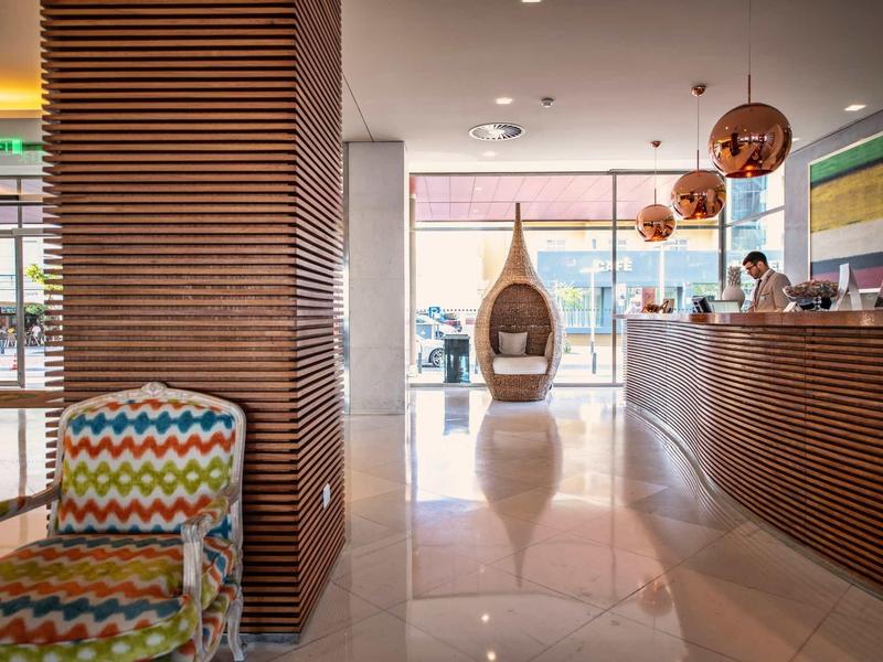 Hall d'hôtel moderne avec espaces assis élégants, réception et grandes fenêtres donnant sur l'extérieur.