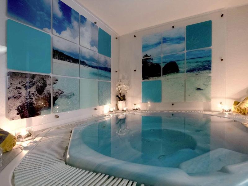Espace intérieur avec jacuzzi rond et grandes images de plage et mer aux murs.