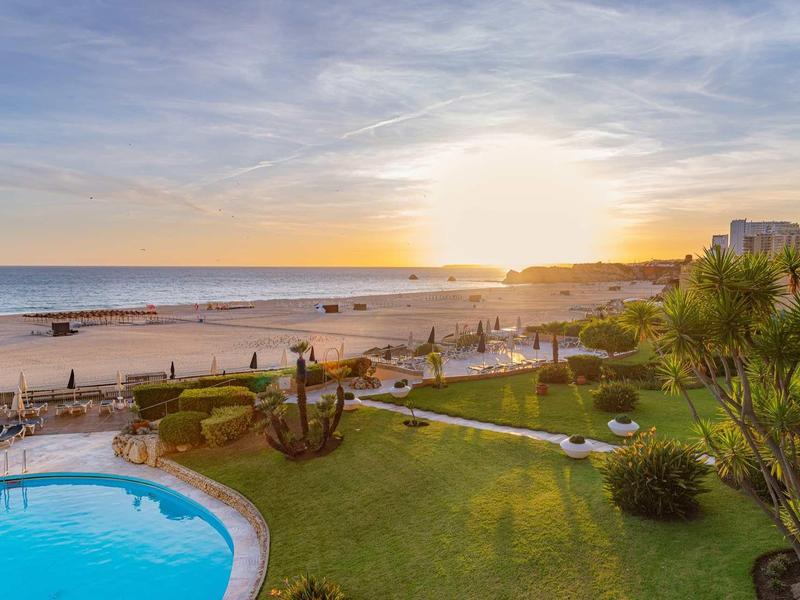 Plage au coucher du soleil avec piscine et jardins verts bien entretenus près des hôtels.