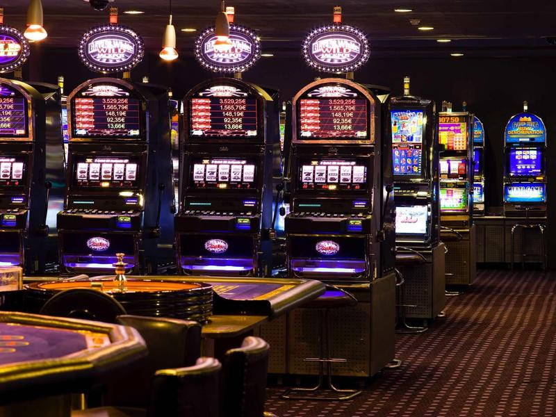 Rangée de machines à sous et table de roulette dans un casino à l'éclairage tamisé.